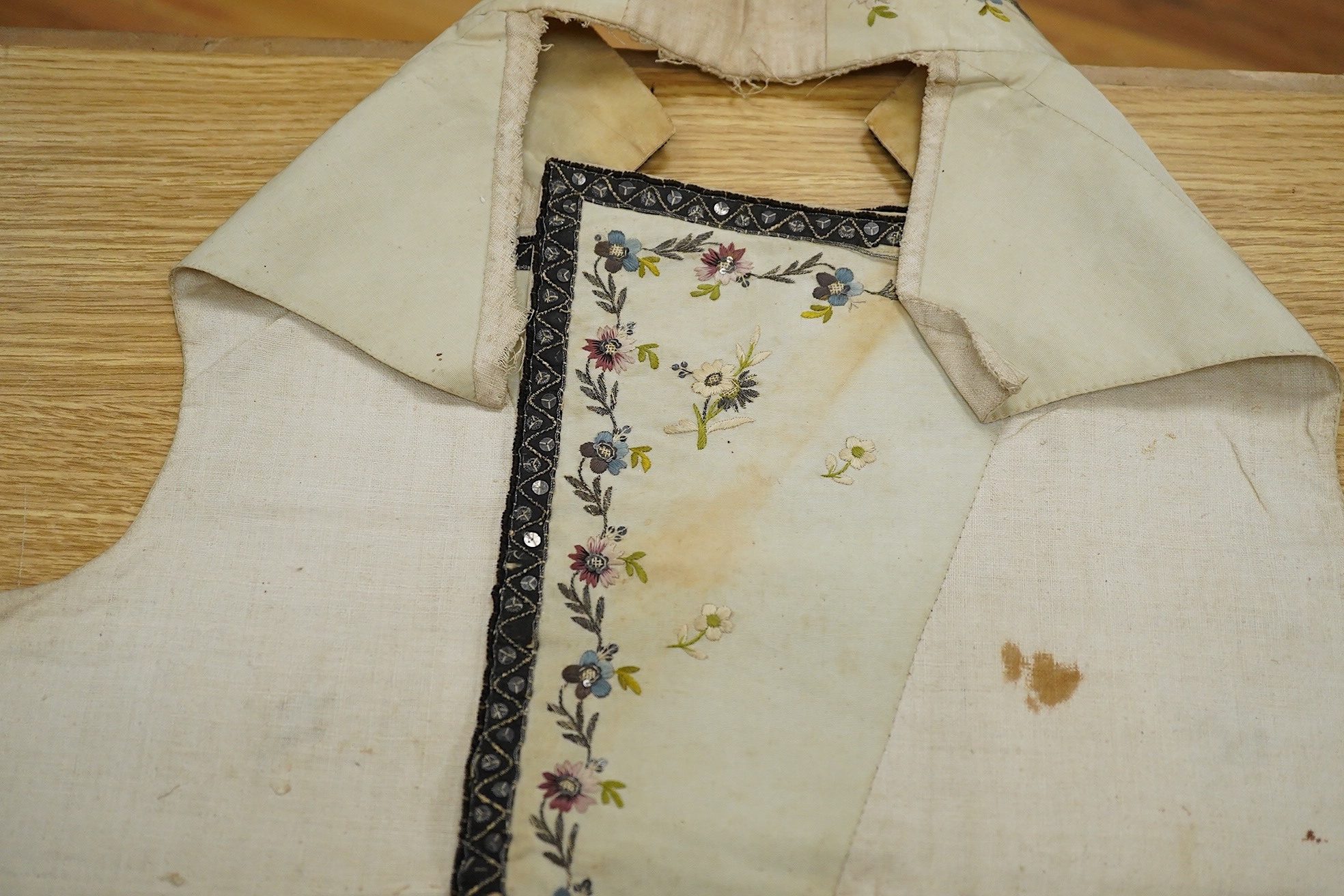 A late George III / George IV gentleman’s cream silk embroidered and cut steel waistcoat front, finely embroidered with polychrome flowers and cut steel appliqués on wide lapels, panel fronts and stand up collar, edged w